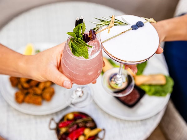 holding fruity cocktails atop a dining table at Soleil Pool Bar