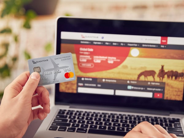 holding a Qantas Premier Everyday card in front of a laptop