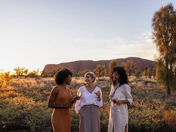 three women drinking champagne in front of uluru