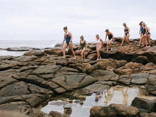 A group of women climb over rocks to the ocean