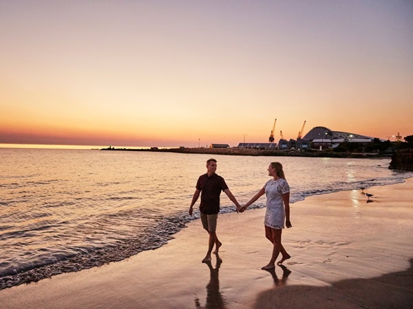 a couple holding hands walking along the Bathers Beach at sunset