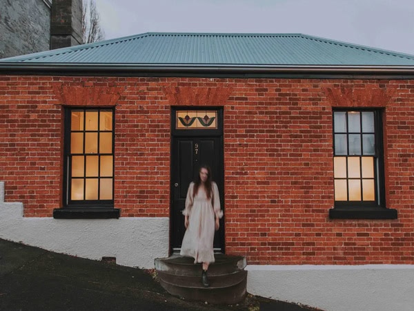 a woman in long white dress stepping out of a brick home at Pickers Cottage