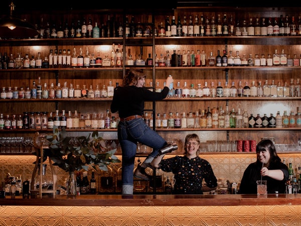 a bartender climbing up a wooden ladder to get a glass bottle at Society Salamanca, Hobart