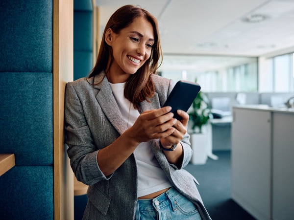 Young happy businesswoman text messaging on cell phone in the office.