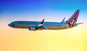 a Boeing 737-800 in Virgin Australia colour scheme taking off from Sydney (Kingsford Smith) Airport on a late afternoon. The plane is bound for Gold coast Queensland