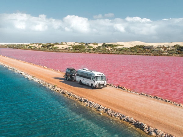 driving on the road between bright blue-green and bright pink waters