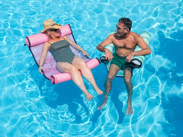 A couple relaxing on the hammocks in a pool.