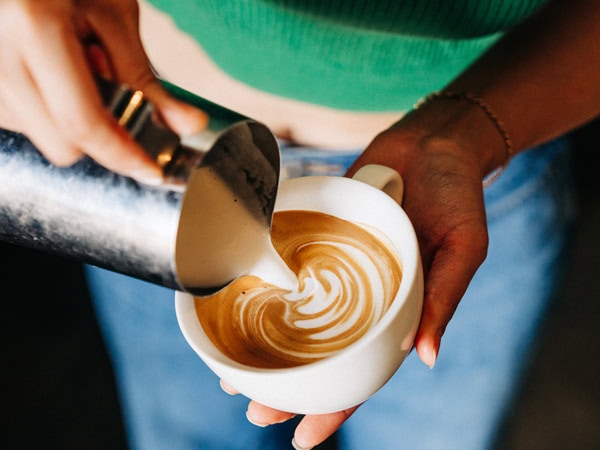 pouring milk into a cup of coffee at Community Coffee Co, Perth