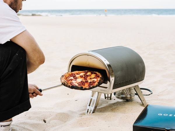 A man making a pizza on the beach the Gozney Roccbox 