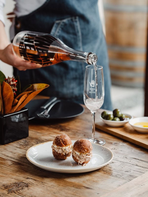 pouring a drink into a glass beside a food plate at LVN Restaurant, Bird in Hand winery