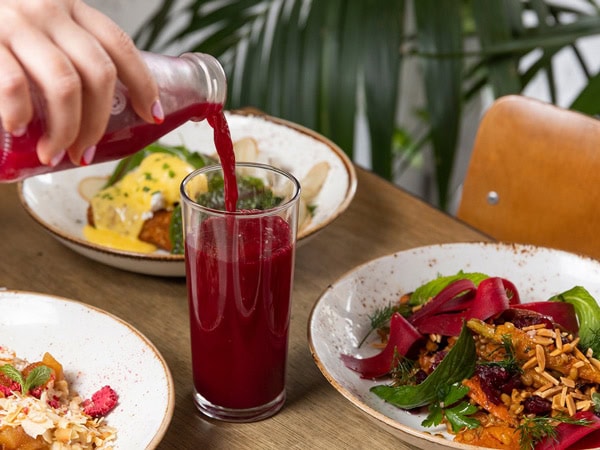a hand pouring a red drink into a glass beside breakfast plates at Mary Street Bakery, Perth