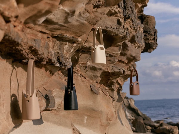 All the colours of mini bags hung on rocks by ocean 