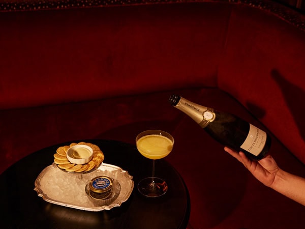 a hand pouring a drink into a glass beside a plate of food on the table at Stan’s Lounge, Howard Smith Wharves