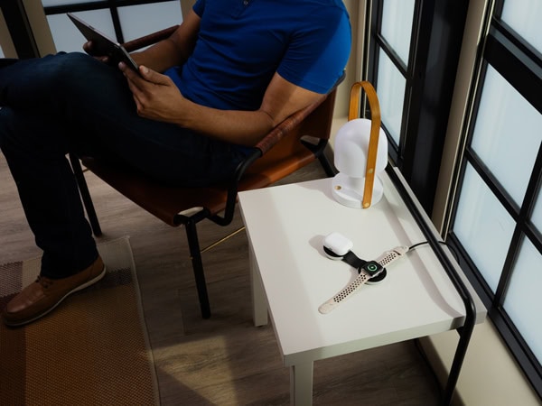 A man on his iPad while charging with apple watch and apple airpod case with the butterfly charger