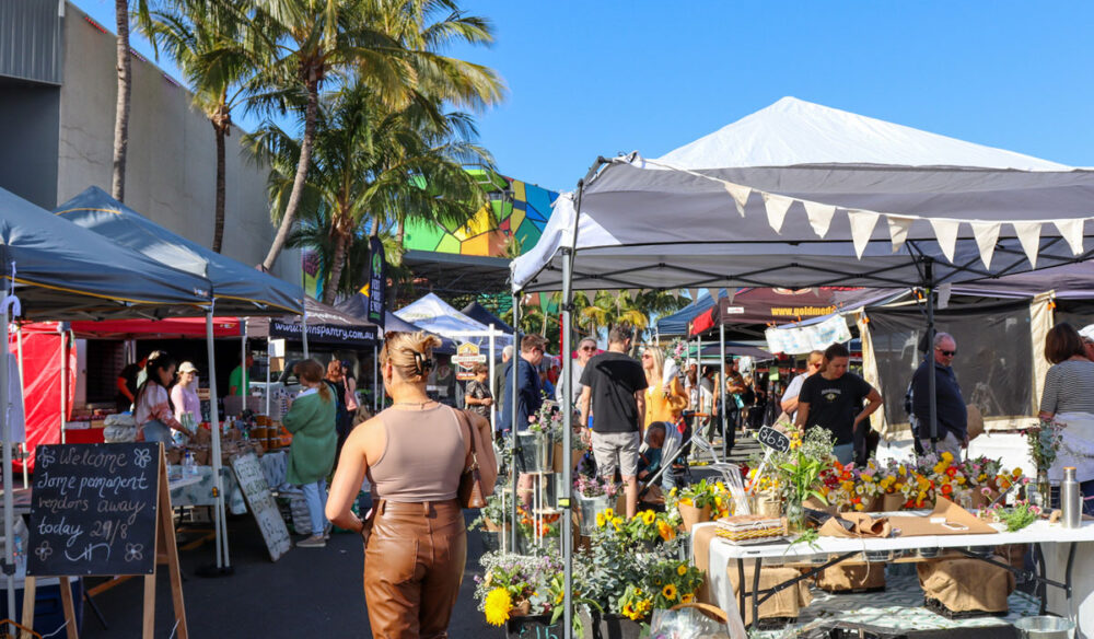 a woman walking in an outdoor market beside a flower stall, HOTA Farmers & Artisan Markets