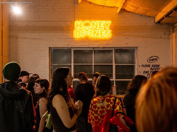 people chatting inside Honey Bones Gallery with a neon-lit signage on the wall, Brunswick