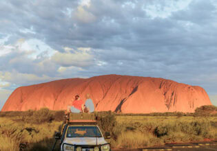 couple sit on top of their car in front of uluru