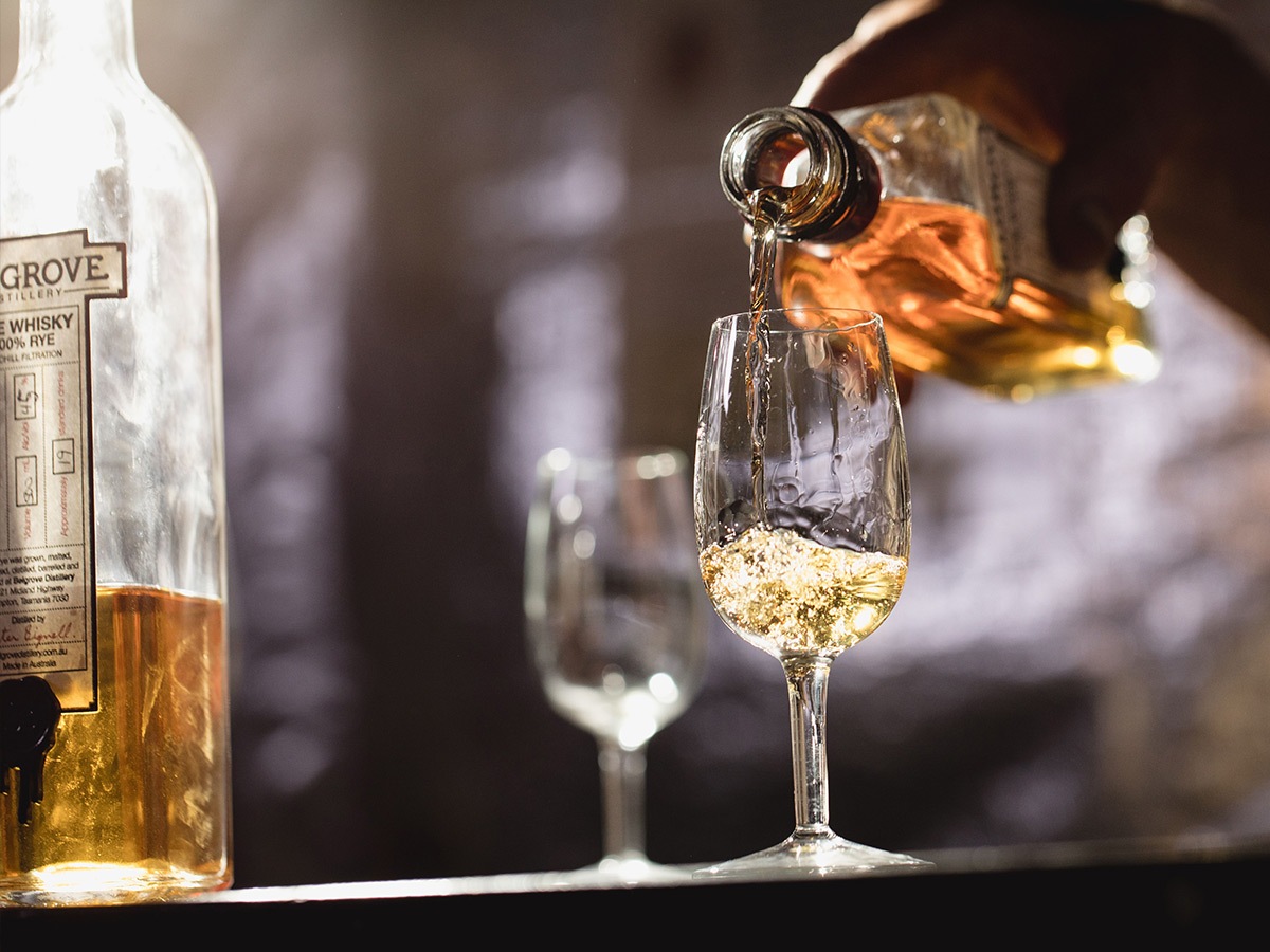 person pouring belgrove distillery whisky into a a glass of ice tasmania