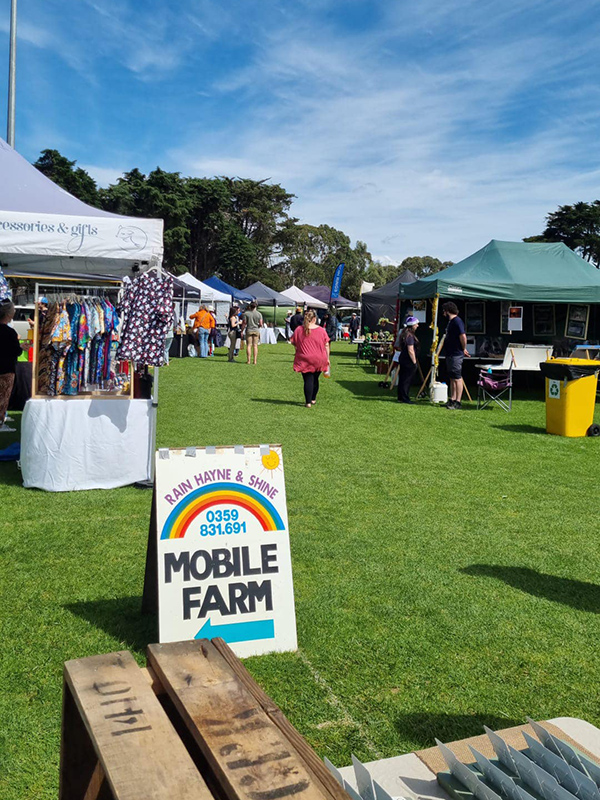 Stalls set up at Boneo Community Market with a sign that leads to the mobile farm.