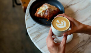 person holiding coffe and croissant in cafe