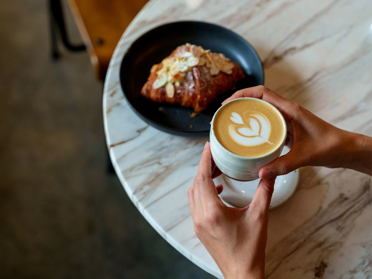 person holiding coffe and croissant in cafe