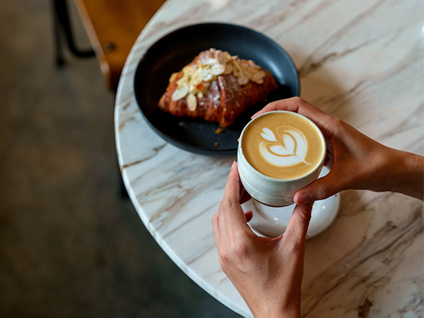 person holiding coffe and croissant in cafe