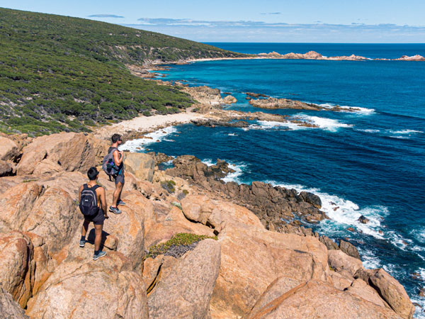 hikers on top of a rocky cliff overlooking a beach in Yallingup