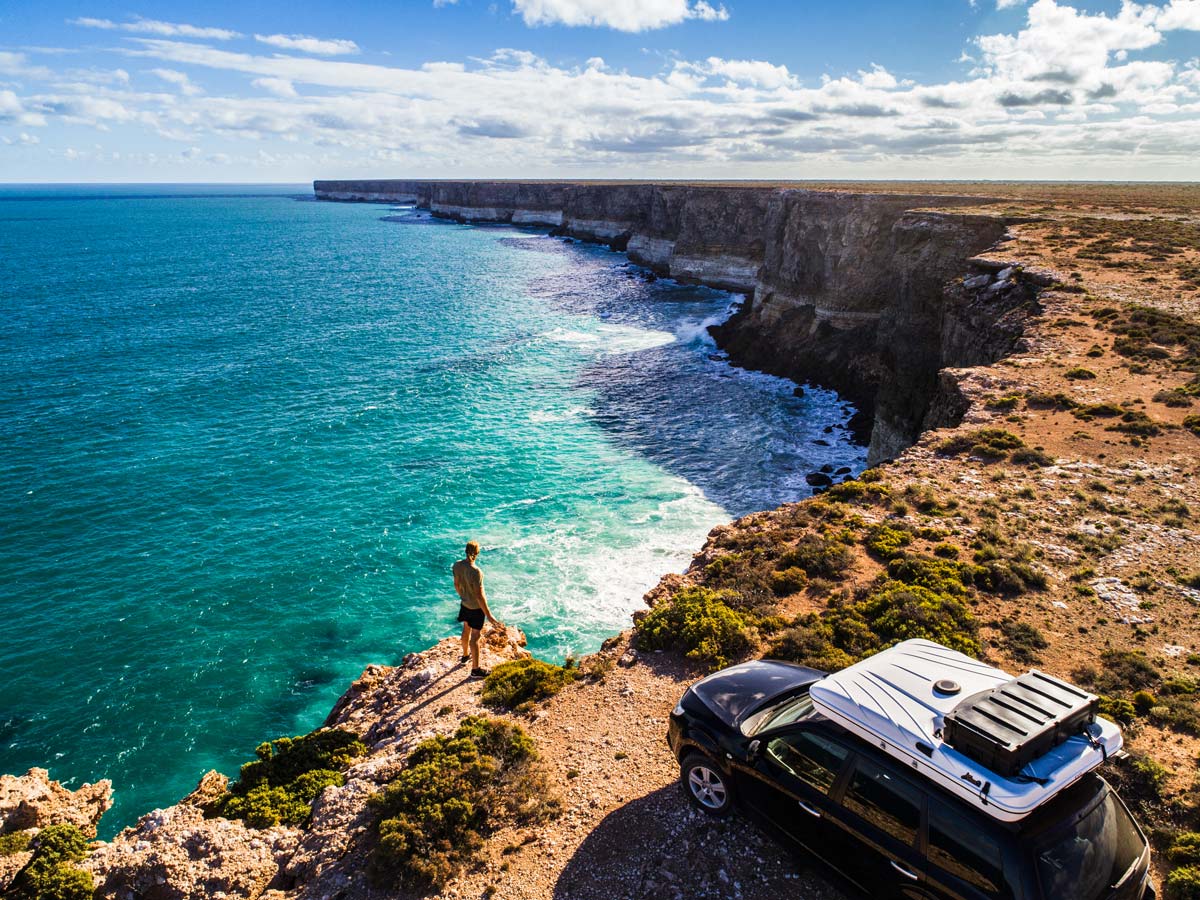 Aerial view of car parked with camper and young man overlooking the Great Australian Bight. Captured while crossing the Nullarbor.