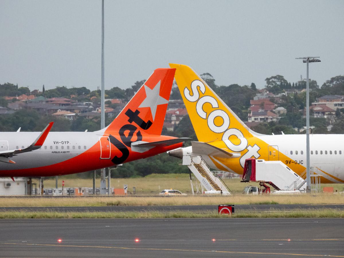 A Jetstar Airbus A321-251NX plane, registration VH-OYP, taxiing at Sydney Kingsford Smith Airport for departure as flight JQ37 to Denpasar. She is passing a Scoot Boeing B787-9 plane, registration 9V-OJC