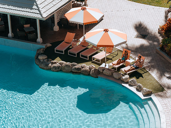 two people in deck chairs by Novotel Cairns Oasis' lagoon-style pool