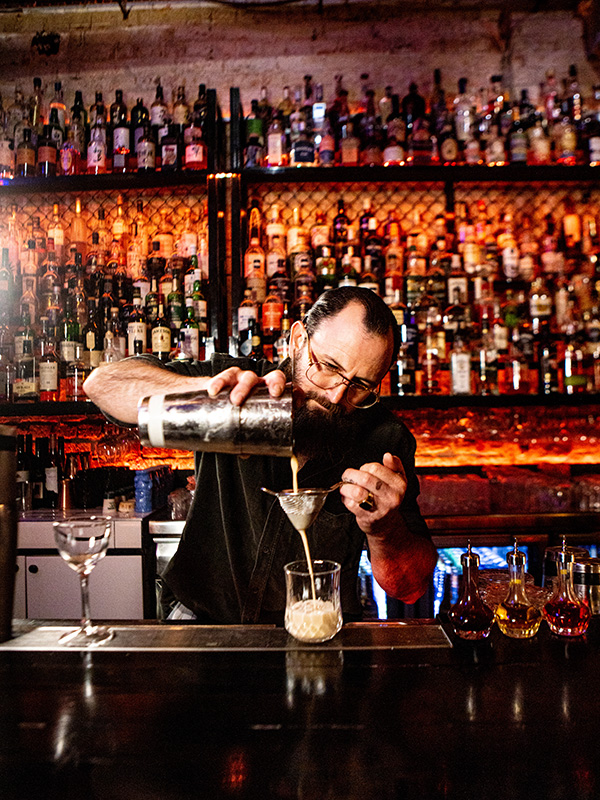 A bartender expertly crafting a drink, with a stunning library of spirits in the background.
