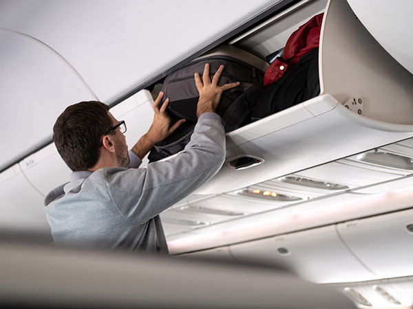 man putting luggage in storage bin on plane