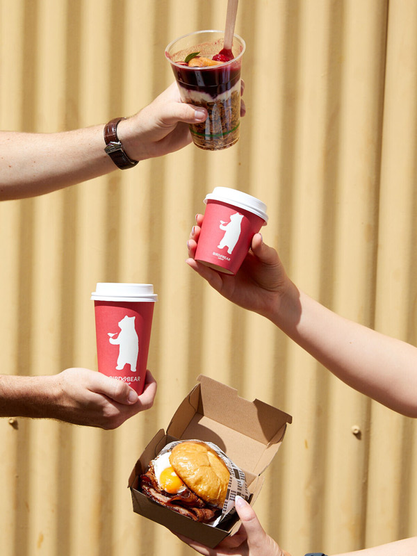 hands holding coffee and burger at Flying Bear, Sydney