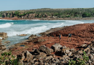 Two people walking on the rocky shoreline near the ocean. Light to Light walk