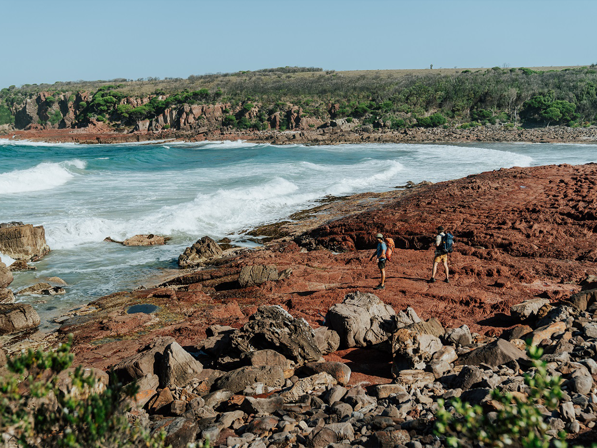 Two people walking on the rocky shoreline near the ocean. Light to Light walk