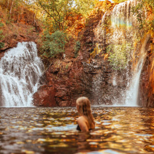 Surrounded by lush forest, a woman cools off in Florence Falls, just one of many incredible things to do in the Northern Territory.