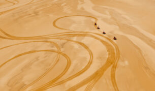 Four rugged 4WDs kick up trails of golden dust as they charge across the sweeping desert landscape.