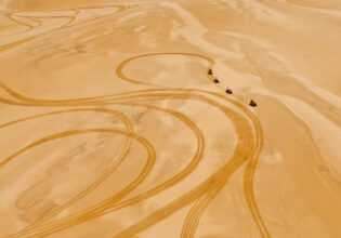 Four rugged 4WDs kick up trails of golden dust as they charge across the sweeping desert landscape.