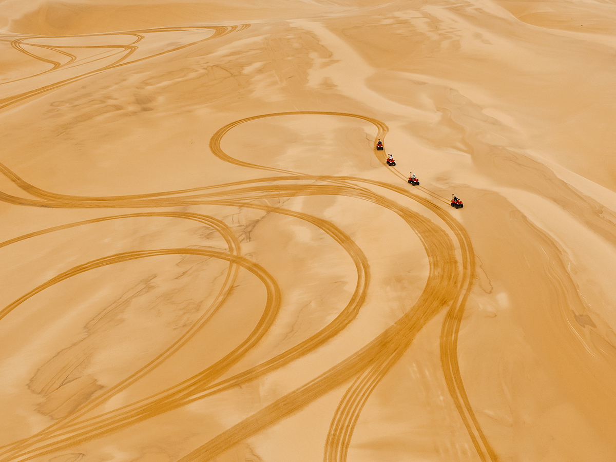 Four rugged 4WDs kick up trails of golden dust as they charge across the sweeping desert landscape.