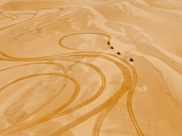 Four rugged 4WDs kick up trails of golden dust as they charge across the sweeping desert landscape. 